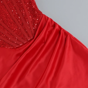 Détail de la broderie de paillettes rouges et du tissu satiné plissé sur la robe de soirée