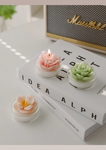 Macro shot of three flower-shaped scented candles in pink and green on a white book