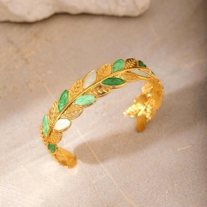 Detail of gold-plated open bangle featuring green and white enamel leaf patterns