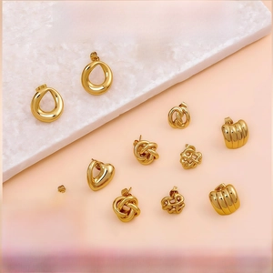 Flat lay of diverse gold geometric stud earrings on a marble board and pink background