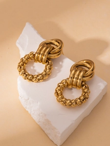 Detailed view of gold door-knocker earrings on white stones with polished metallic finish