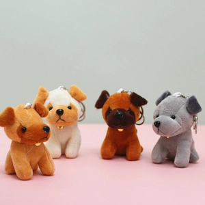Close-up of four plush puppy keychains with golden bells on a pink and grey background