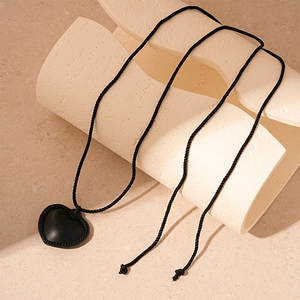 Close-up of black leather heart pendant with woven edge on minimalist stone display