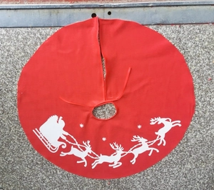 Detail of red Christmas tree skirt with white reindeer and Santa print on fabric