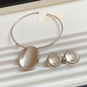 Close-up of silver metal jewelry set with oval pendant necklace and round stud earrings