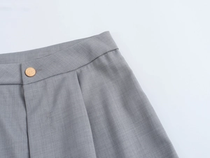 Détail d'un pantalon gris clair avec taille haute plissée et bouton doré élégant