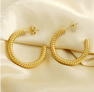 Macro detail of gold-plated twisted hoop earrings on a luxury satin background