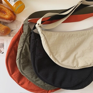 Flat lay of half-moon nylon crossbody bags in four colors with casual lifestyle props