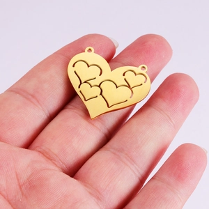 Gold hollow heart pendant with small heart cutouts held by hand on pink backdrop
