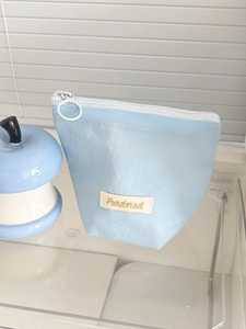 Light blue nylon pouch with metal ring zipper and woven label detail on textured fabric