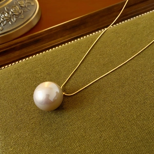 Close-up of gold snake chain with large round pearl pendant on green textured fabric