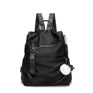 Black nylon backpack with front zipper pocket and white pompom charm on white background