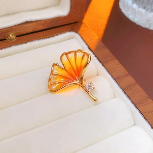 Detailed close-up of a golden ginkgo leaf brooch with orange enamel and a cubic zirconia