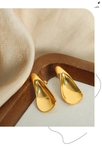 Macro view of gold-plated curved triangular earrings on a dark wood and silk display