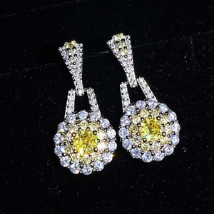 Macro shot of yellow gemstone earrings with white zircon halo on black velvet
