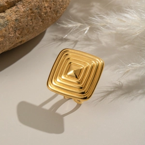 Detailed view of a gold square ring with geometric patterns on a beige stone background