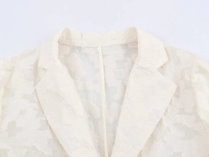Détail du blazer en dentelle blanc cassé montrant la texture jacquard et le col à revers