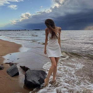 Close-up of white slim fit strap mini dress against a scenic seaside beach background