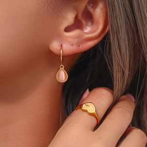 Close-up of gold water drop pink cat-eye stone earrings and Mom heart ring on model