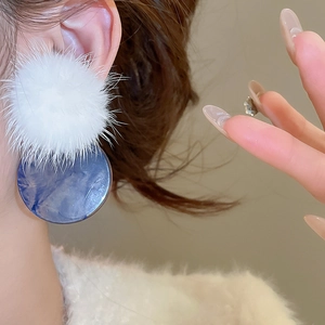 Close-up of white fur ball and marble blue round pendant earrings worn on ear
