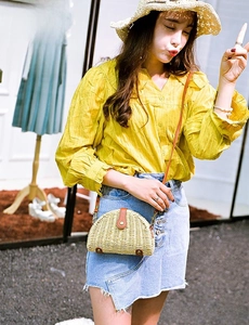 Detail of semi-circular straw crossbody bag with brown leather strap and buckle