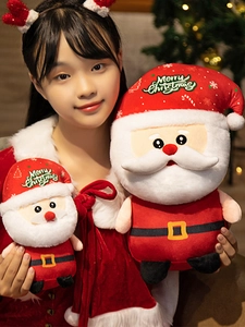 Detail showing two sizes of Santa Claus plush dolls held by a model near a Christmas tree