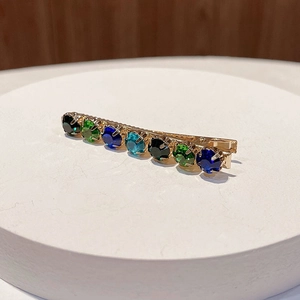 Detail of elegant gold alloy hair clip with colorful gemstones on a white pedestal