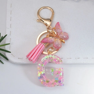 Macro shot of resin letter G keychain with pink butterfly sequins and gold tassel details