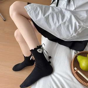 Black crew socks with ruffled edges, lace hearts, and cute bows in a cozy home setting