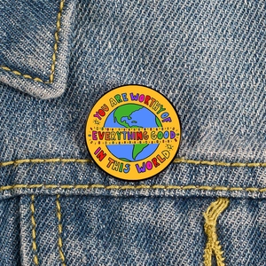 Macro detail of round enamel mental health pin on denim with inspirational quote