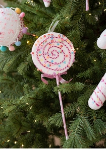 Pink and white candy cane ornaments hanging on a green Christmas tree with warm lights