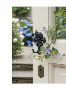 Detail of vintage black cast iron fleur-de-lis hook on wooden door with garden backdrop