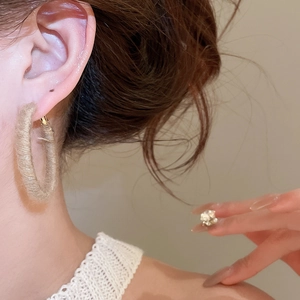 Detailed view of beige woven rope hoop earring with bohemian texture on model