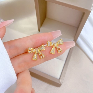 Close-up of gold bow earrings with clear zircons being held to show fine jewelry detail