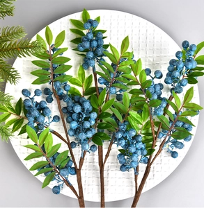 Close-up of artificial blue berry stems with green leaves on a white texture plate