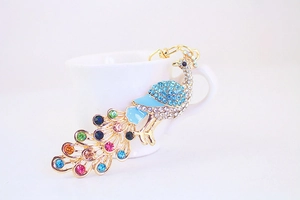 Macro shot of colorful rhinestone peacock keychain resting on a white ceramic cup