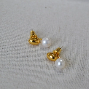 Detailed view of gold plated brass studs with white freshwater pearls on white fabric