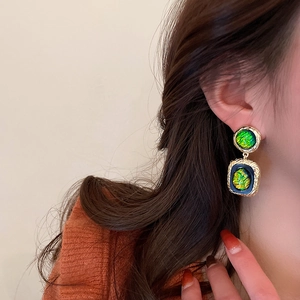 Macro detail of vintage geometric gold-rimmed earrings with emerald green resin inlay