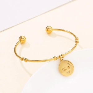 Macro detail of polished gold smiley face charm on minimalist stainless steel bangle