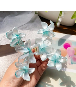 Detail showing a gradient blue flower hair claw clip held by hand against soft fabrics