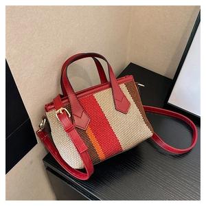 Detail of red leather straps on a striped woven canvas tote bag over dark wood