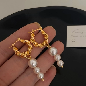 Detail of twisted gold metal hoop earrings with three vertical gradient white pearls