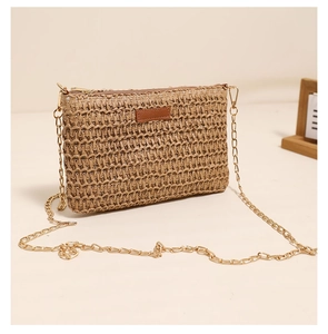 Detail of khaki straw woven crossbody bag with golden chain strap and leather patch