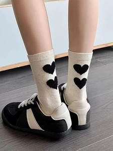 Detail of cream white mid-calf socks featuring black heart patterns and ribbed cuffs
