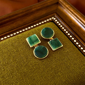 Detail of asymmetrical green marble resin earrings with gold metal accents on fabric