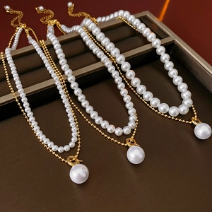 Detail of layered gold-plated chain and white pearl necklace on dark display tray