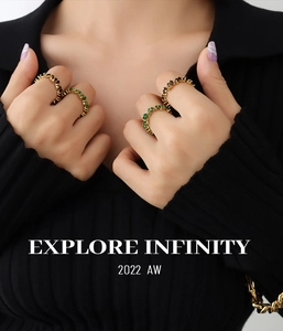 Close-up of stacked gold rings with emerald and black gemstones on a black sweater