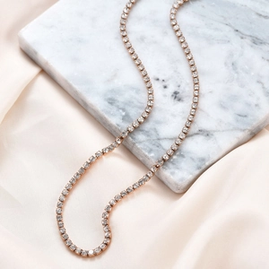 Detail der roségoldenen Tenniskette mit klaren Kristallen auf Marmor und Seide