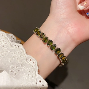 Close-up of olive green pear-cut gemstone bracelet on a wrist with white lace sleeves