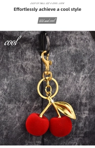Detail of red velvet cherry bag charm with golden metal leaves on denim background